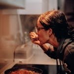 Woman cooking and tasting a dish on the stove, showcasing home culinary expertise.